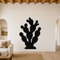 Black metal prickly pear cactus wall art with multiple segmented pads and cutout details, mounted on a white living room wall above a beige sofa.