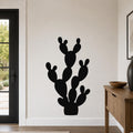 Black metal wall art in the silhouette of a prickly pear cactus, mounted on a white wall in a modern entryway.