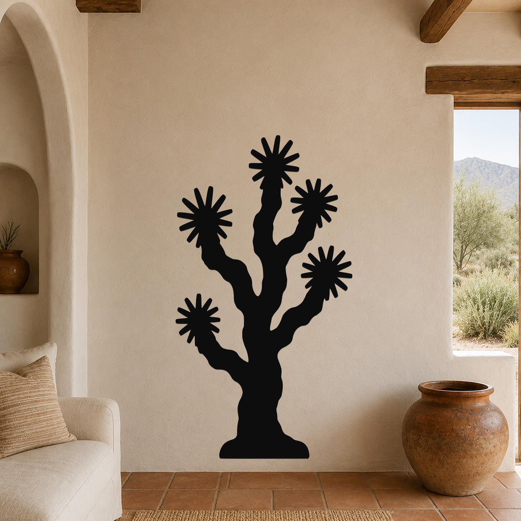 Black metal Joshua tree wall art with starburst cutouts, mounted on a beige stucco wall in a living room with terracotta flooring and wooden beams.
