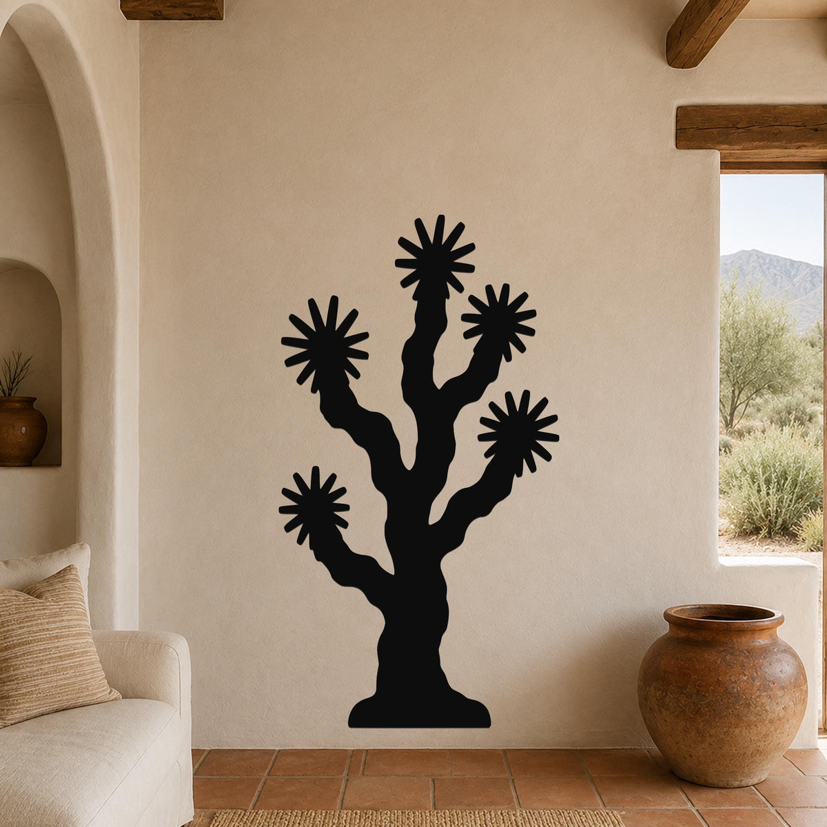 Black metal Joshua tree wall art with starburst cutouts, mounted on a beige stucco wall in a living room with terracotta flooring and wooden beams.