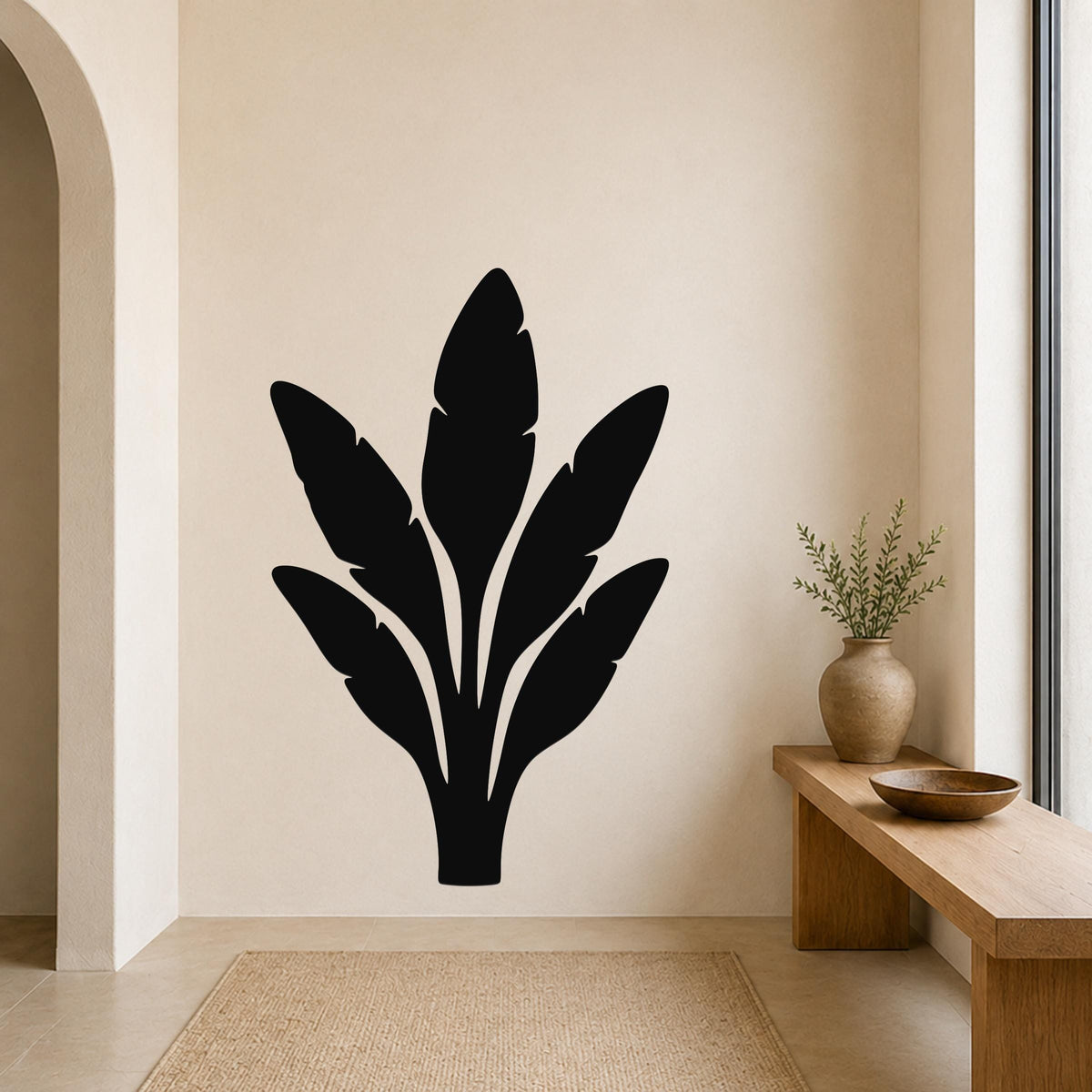 Black metal wall art in a banana leaf silhouette design, mounted on a beige wall above a wooden bench in a minimalist entryway.
