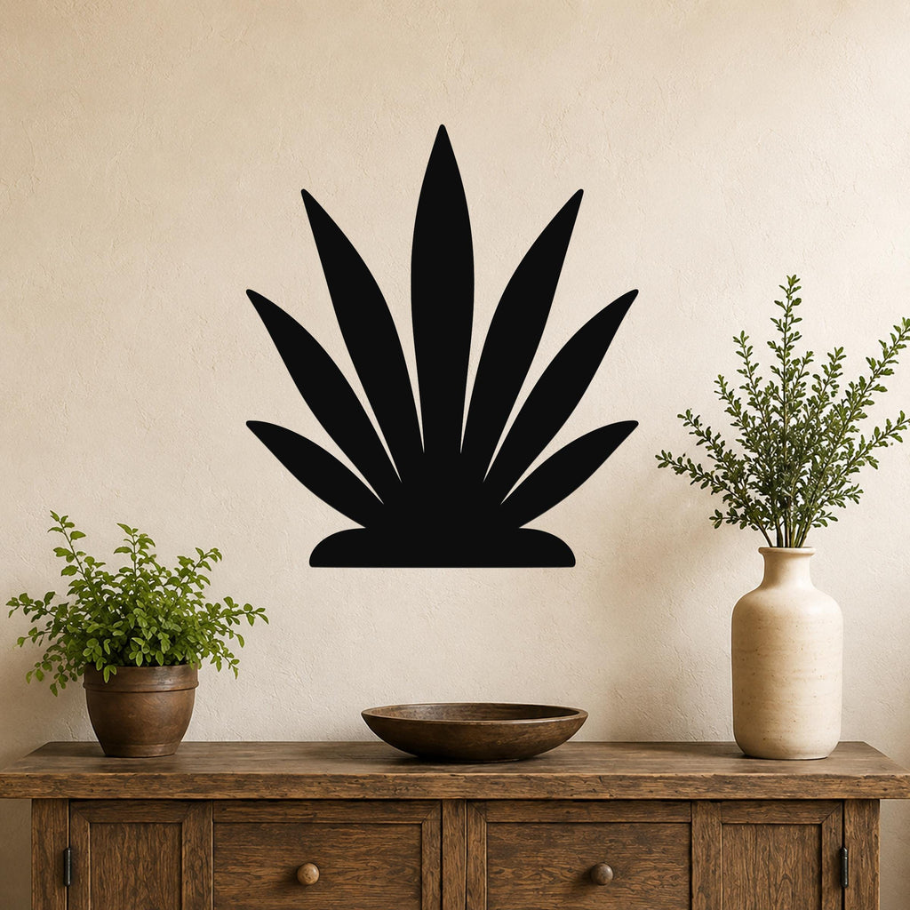 Black metal agave wall art silhouette with pointed leaves, mounted on a beige wall above a wooden console table with potted plants.