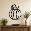 Black metal barrel cactus wall art with flower and spine cutouts, mounted on a beige wall above a wooden console table.