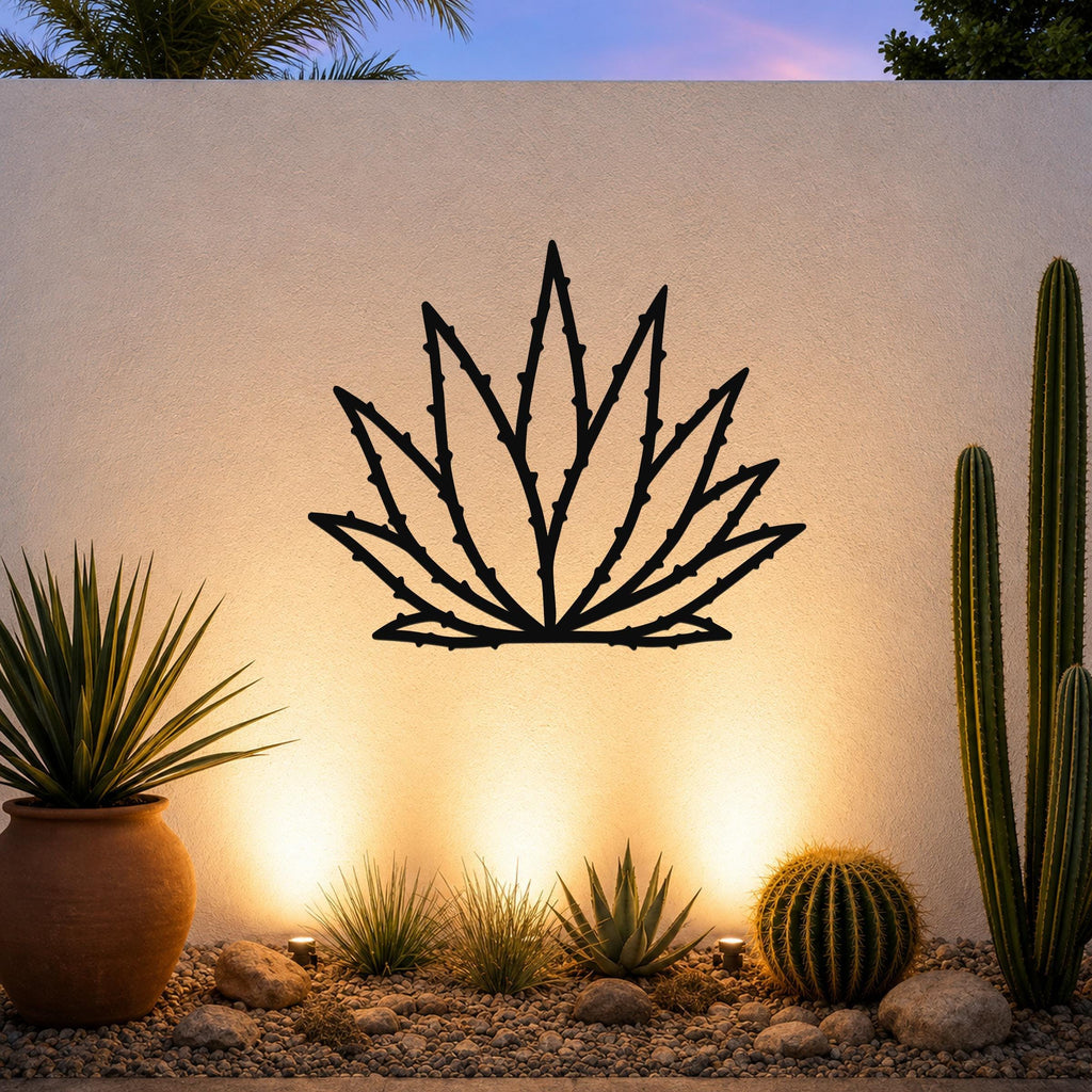 Black metal agave wall art with spiky leaf cutouts, mounted on a textured outdoor wall above a desert garden with cacti and warm uplighting.