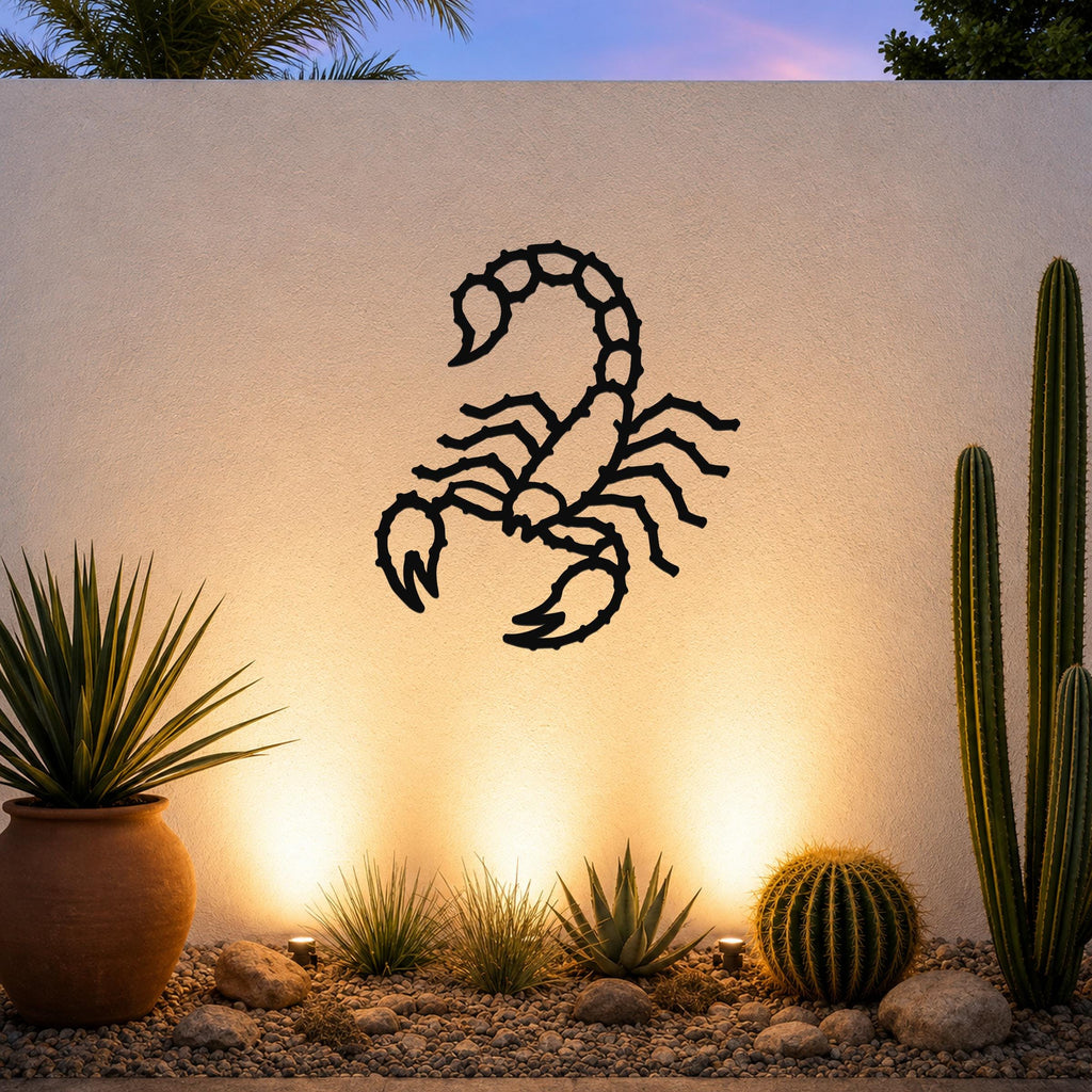 Black metal scorpion wall art with detailed cutout design, mounted on a textured outdoor wall above a desert garden with cacti and warm uplighting.