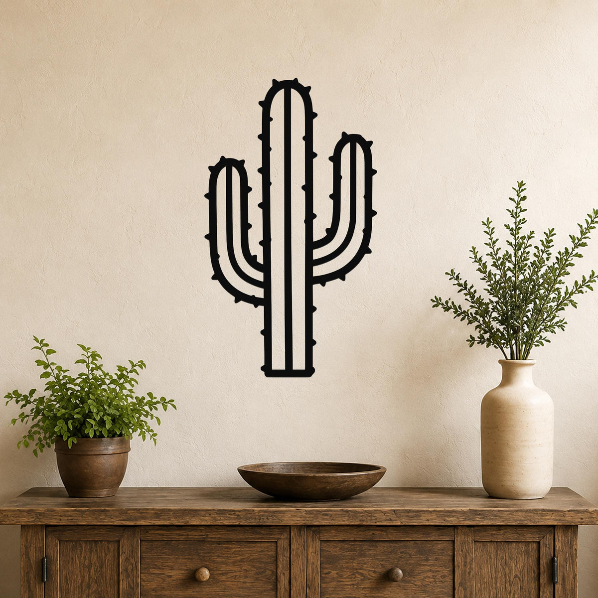Black metal wall art in the silhouette of a saguaro cactus with spines and arms, mounted on a beige wall above a wooden console table.