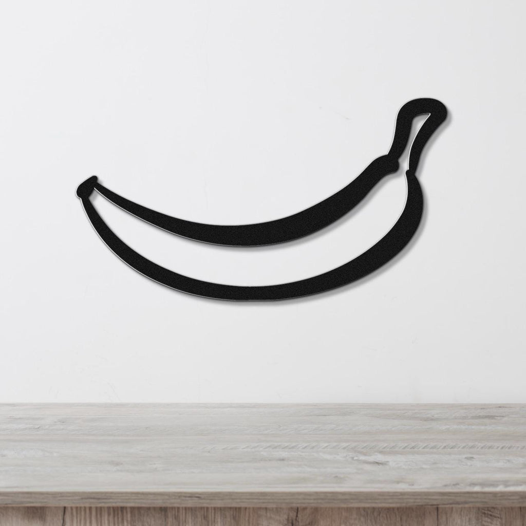 Black metal banana wall art with a clean silhouette design, mounted on a white wall above a light wood countertop.