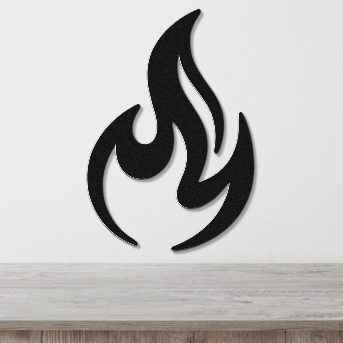 Black metal flame wall art with bold silhouette and internal cutout details, mounted on a white wall above a light wood surface.