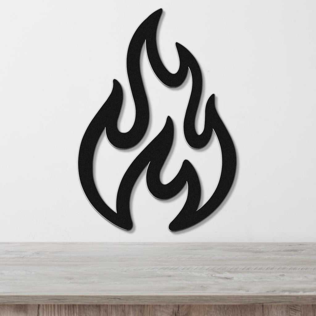 Black metal wall art in a flame silhouette with layered cutouts, mounted on a white wall above a light wood surface.