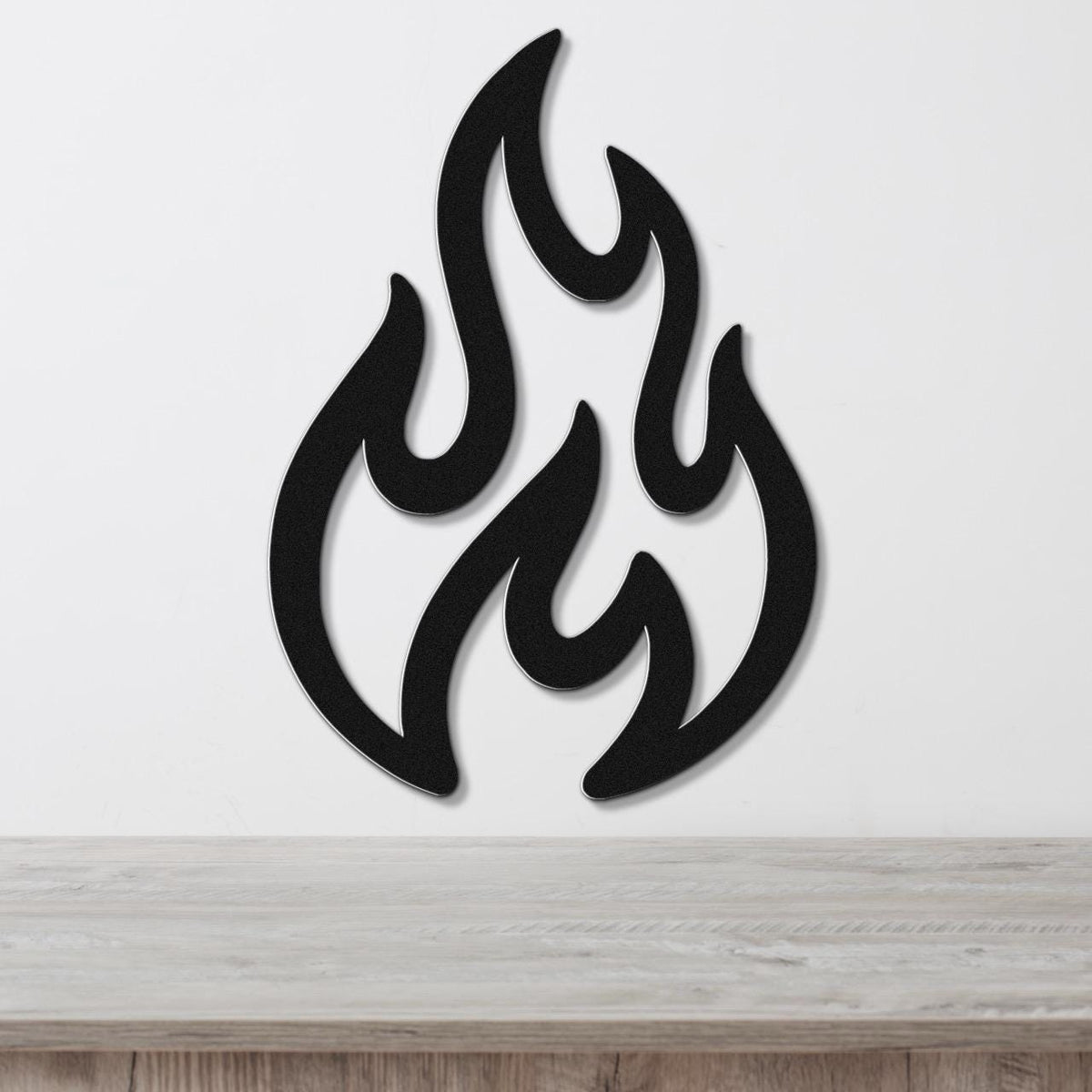 Black metal wall art in a flame silhouette with layered cutouts, mounted on a white wall above a light wood surface.
