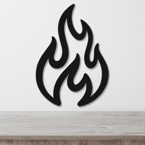 Black metal wall art in a flame silhouette with layered cutouts, mounted on a white wall above a light wood surface.