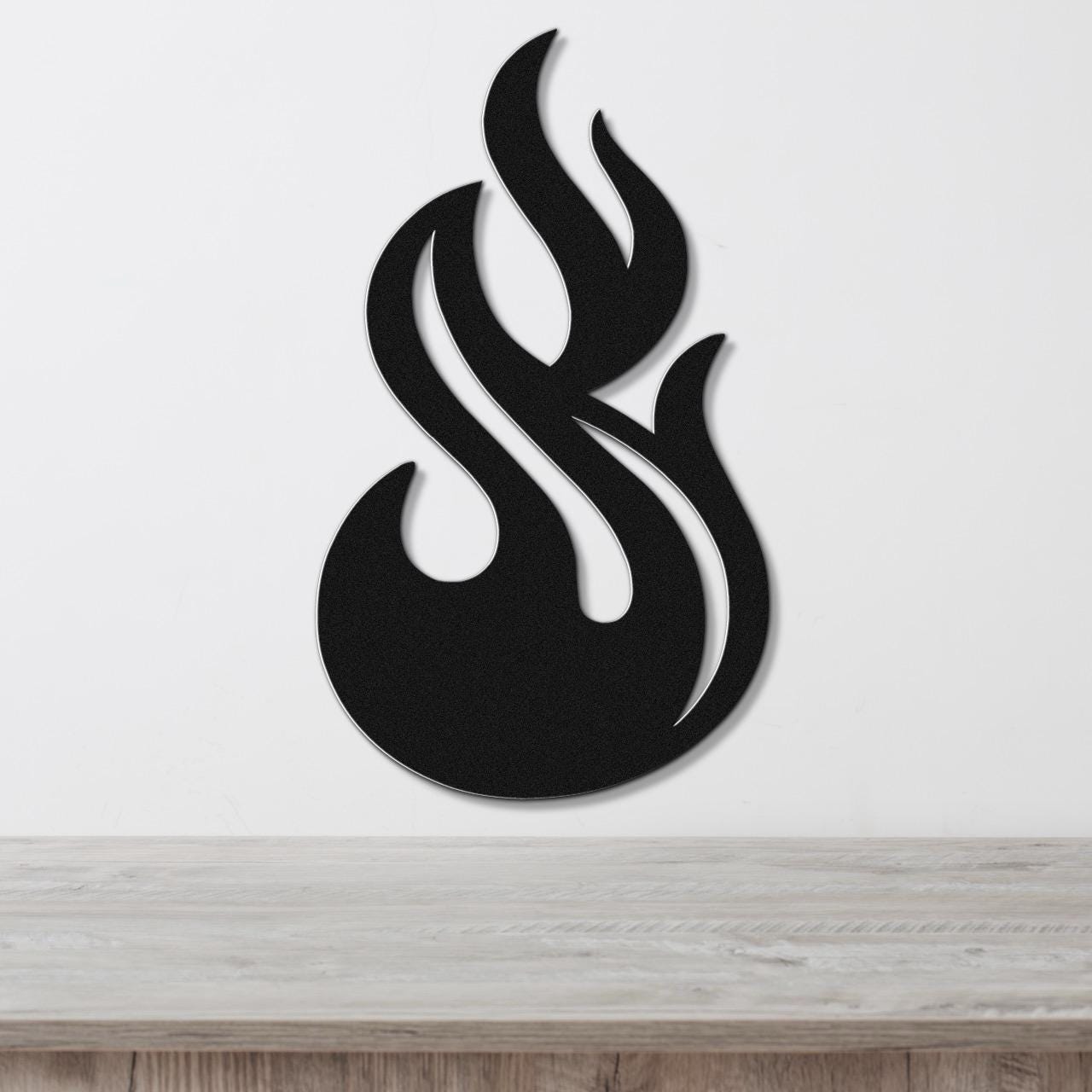 Black metal flame wall art with flowing cutout design, mounted on a white wall above a light wood surface.