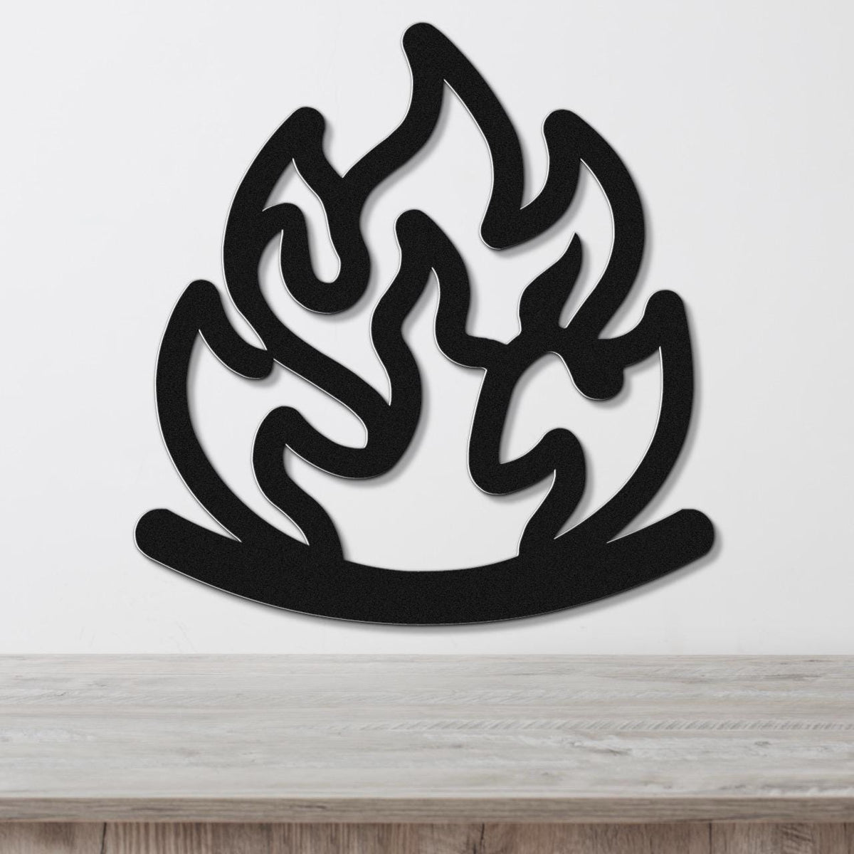 Black metal wall art in a flame silhouette with fluid, swirling cutouts, mounted on a white wall above a light wood surface.