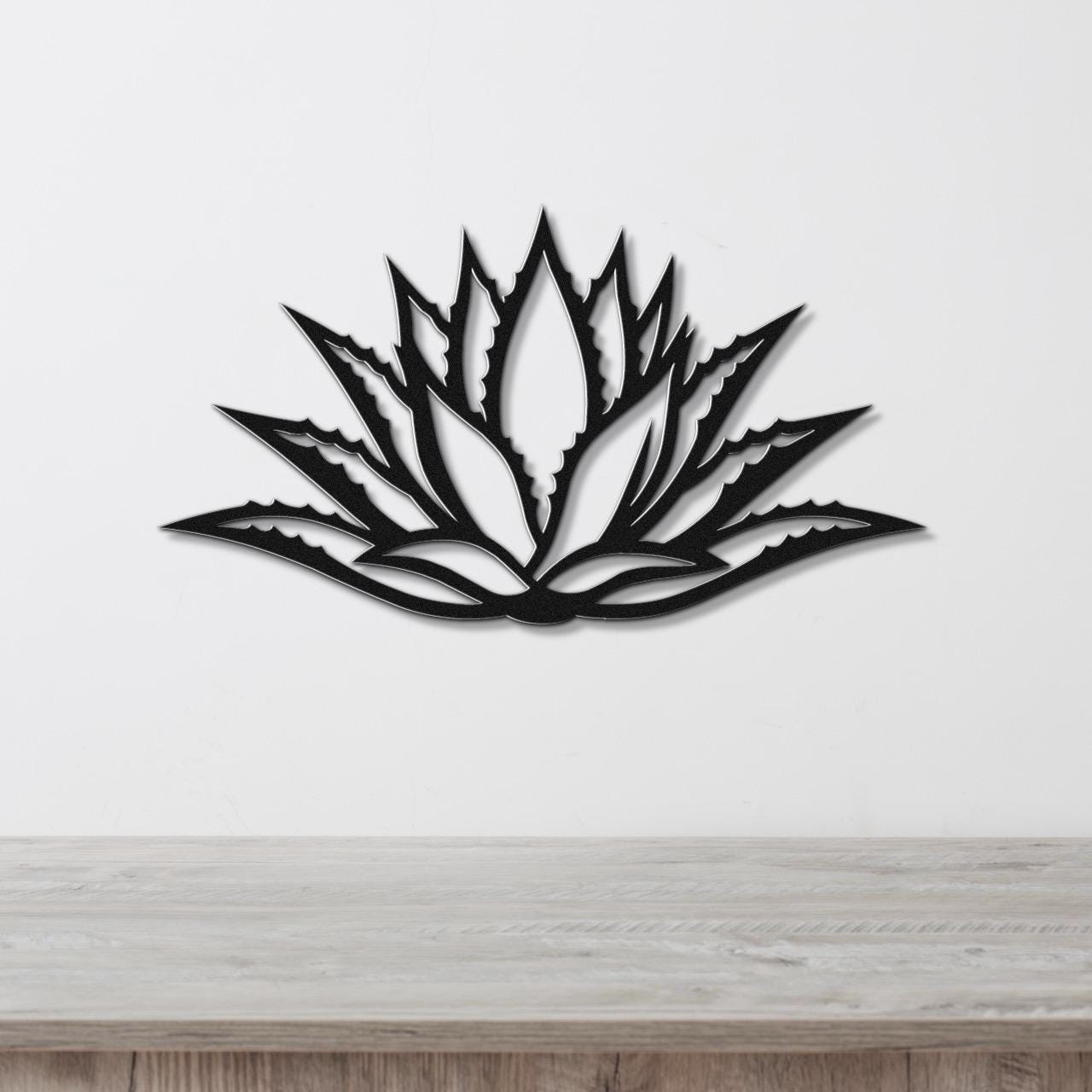 Black metal agave wall art with a bold geometric cutout design, mounted on a white wall above a light wood counter.