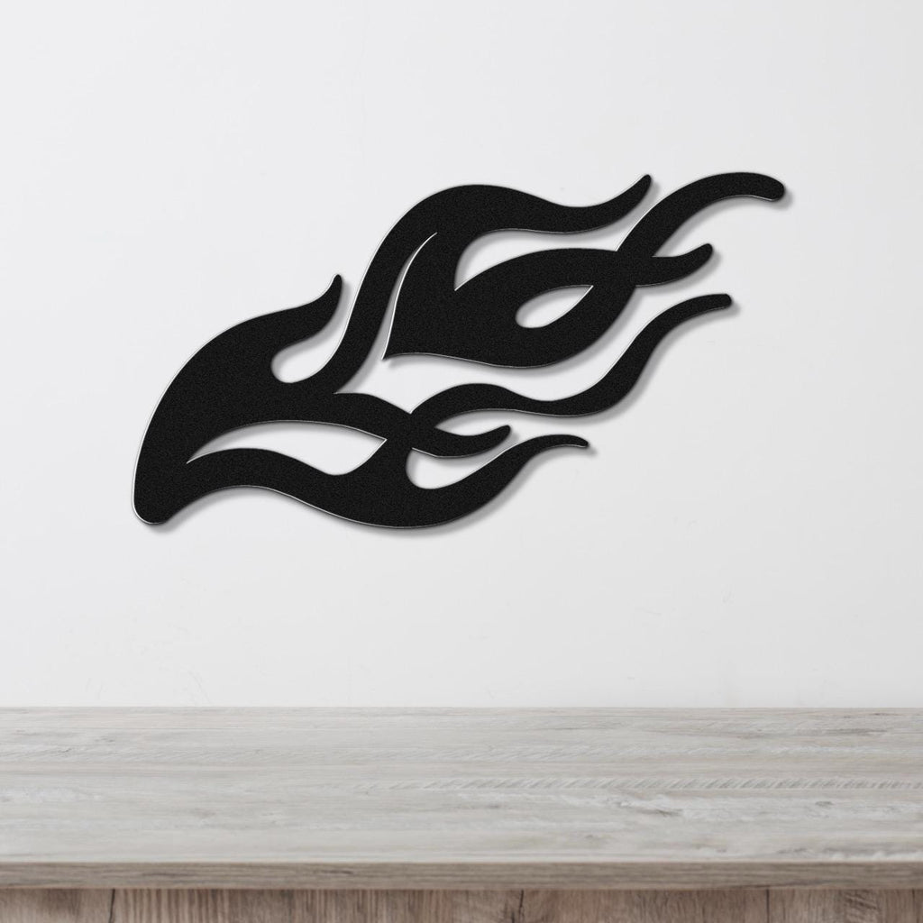 Black metal flame wall art with flowing silhouette cutouts, mounted on a white wall above a light wood surface.