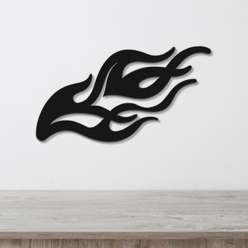 Black metal flame wall art with flowing silhouette cutouts, mounted on a white wall above a light wood surface.