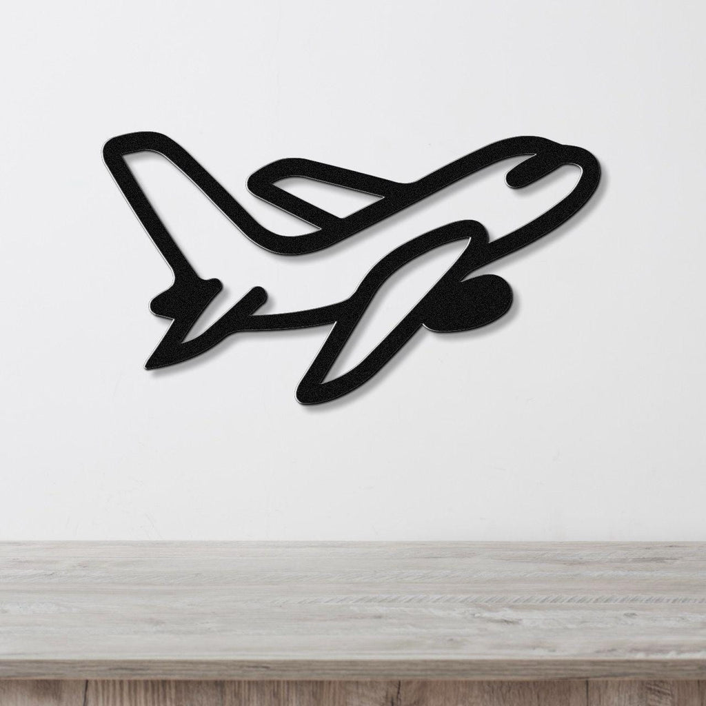 Black metal airplane wall art with a sleek silhouette design, mounted on a white wall above a light wood surface.