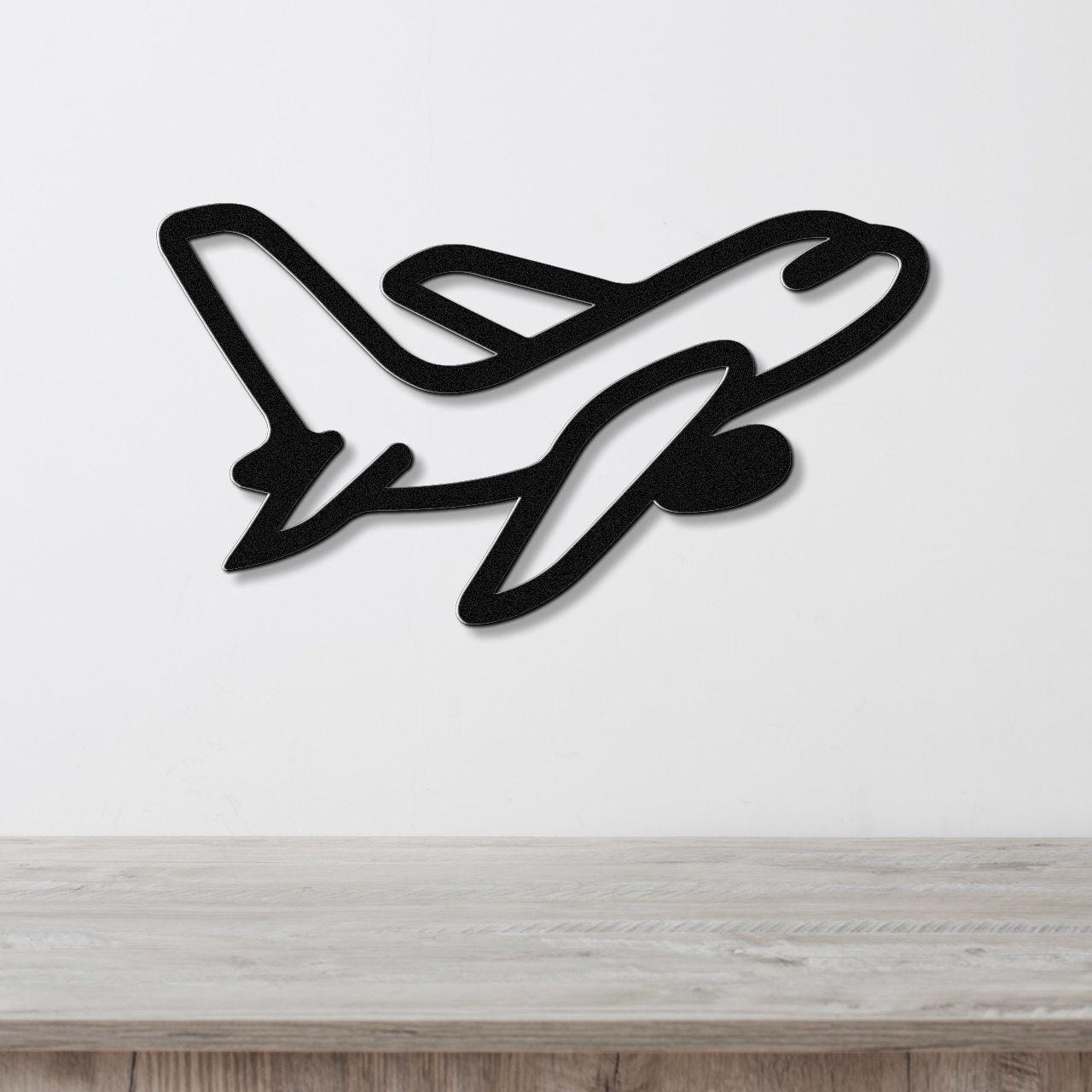 Black metal airplane wall art with a sleek silhouette design, mounted on a white wall above a light wood surface.