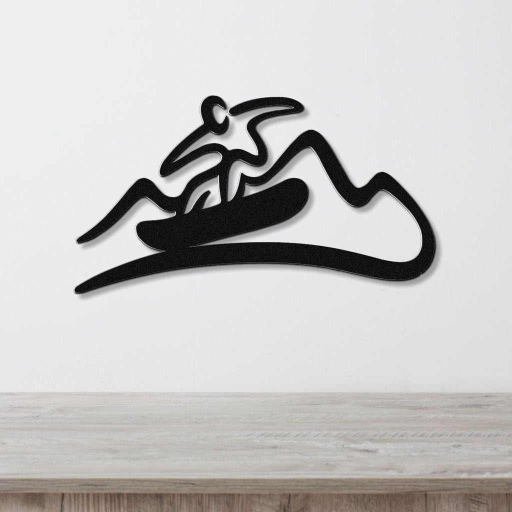 Black metal wall sculpture with a minimalist snowboarder silhouette and mountain cutout design, mounted on a white wall above a wooden counter.