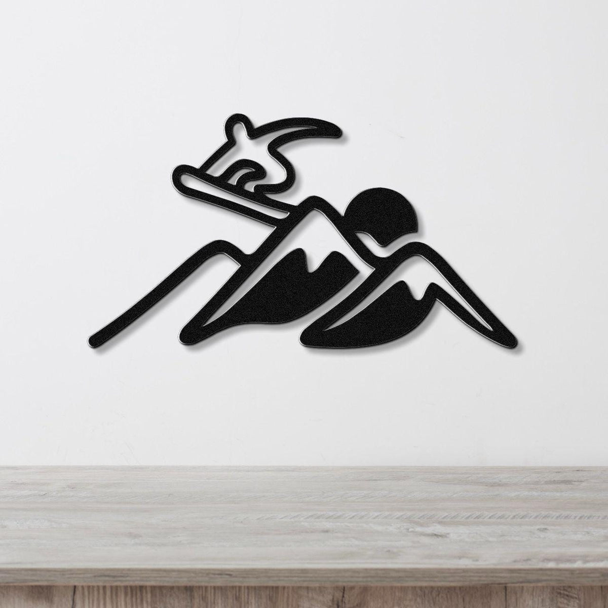 Black metal wall art silhouette of a snowboarder on a mountain, mounted on a white wall above a wooden counter.