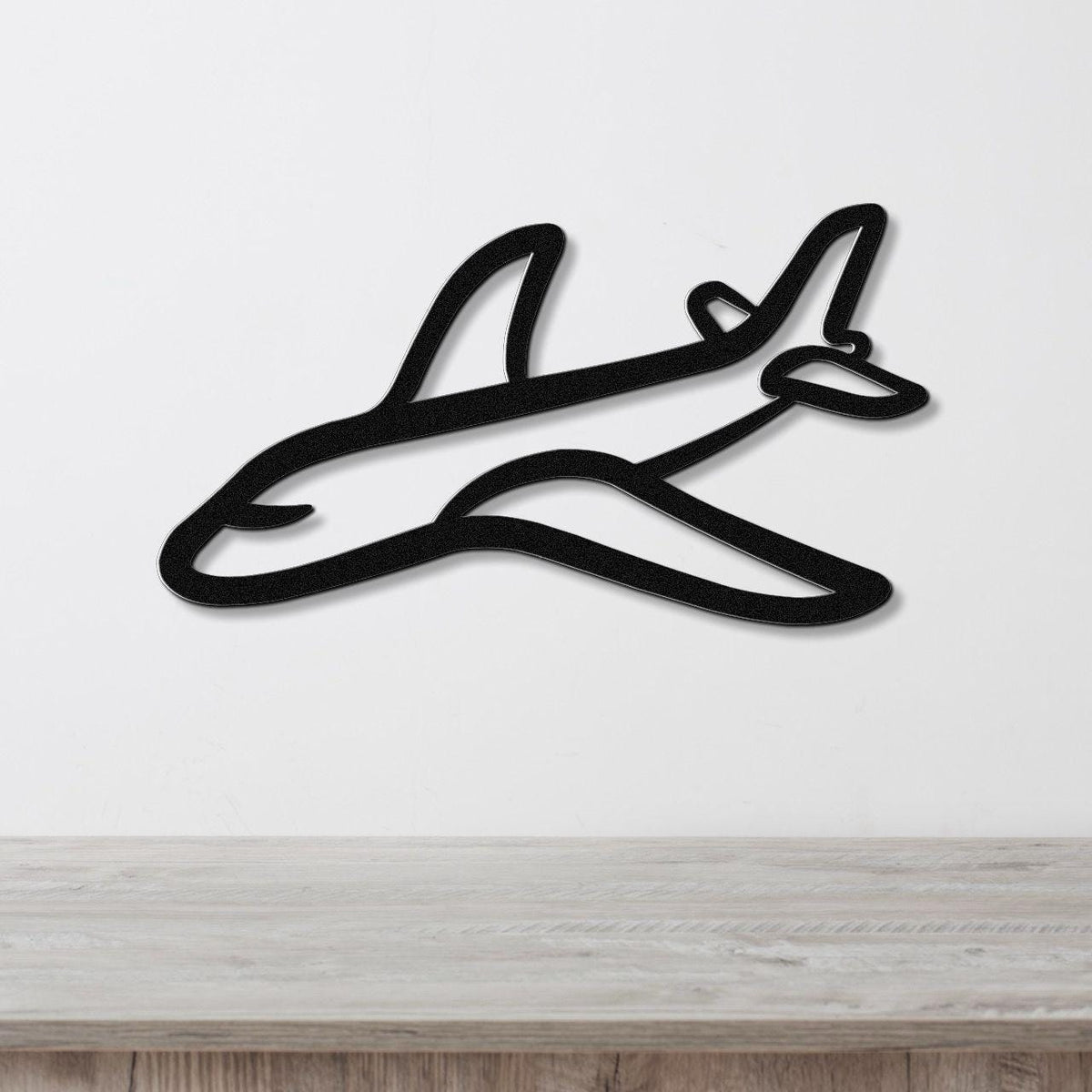 Black metal airplane wall art with a sleek silhouette design, mounted on a white wall above a light wood countertop.