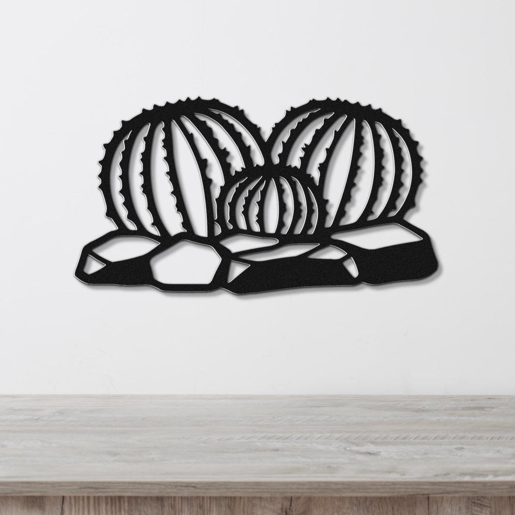 Black metal barrel cactus wall art with ribbed cutout design, mounted on a white wall above a wooden surface.