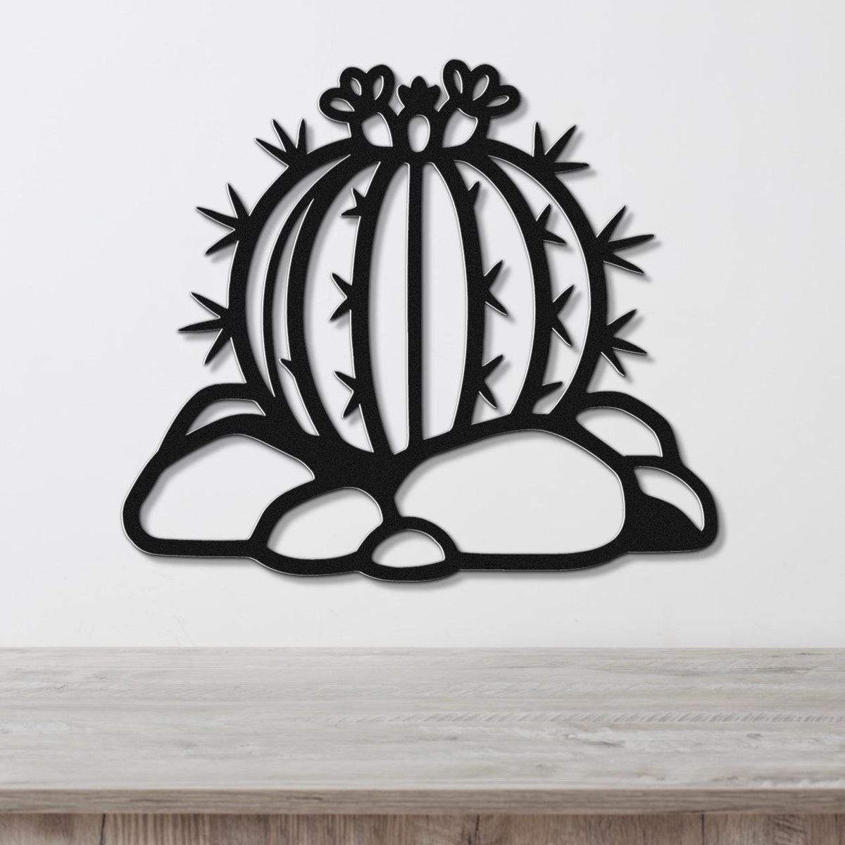 Black metal barrel cactus wall art with flower and spine cutouts, mounted on a white wall above a wooden counter.