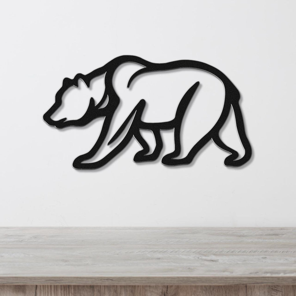 Black metal bear wall art with a silhouette cutout design, mounted on a white wall above a light wood surface.