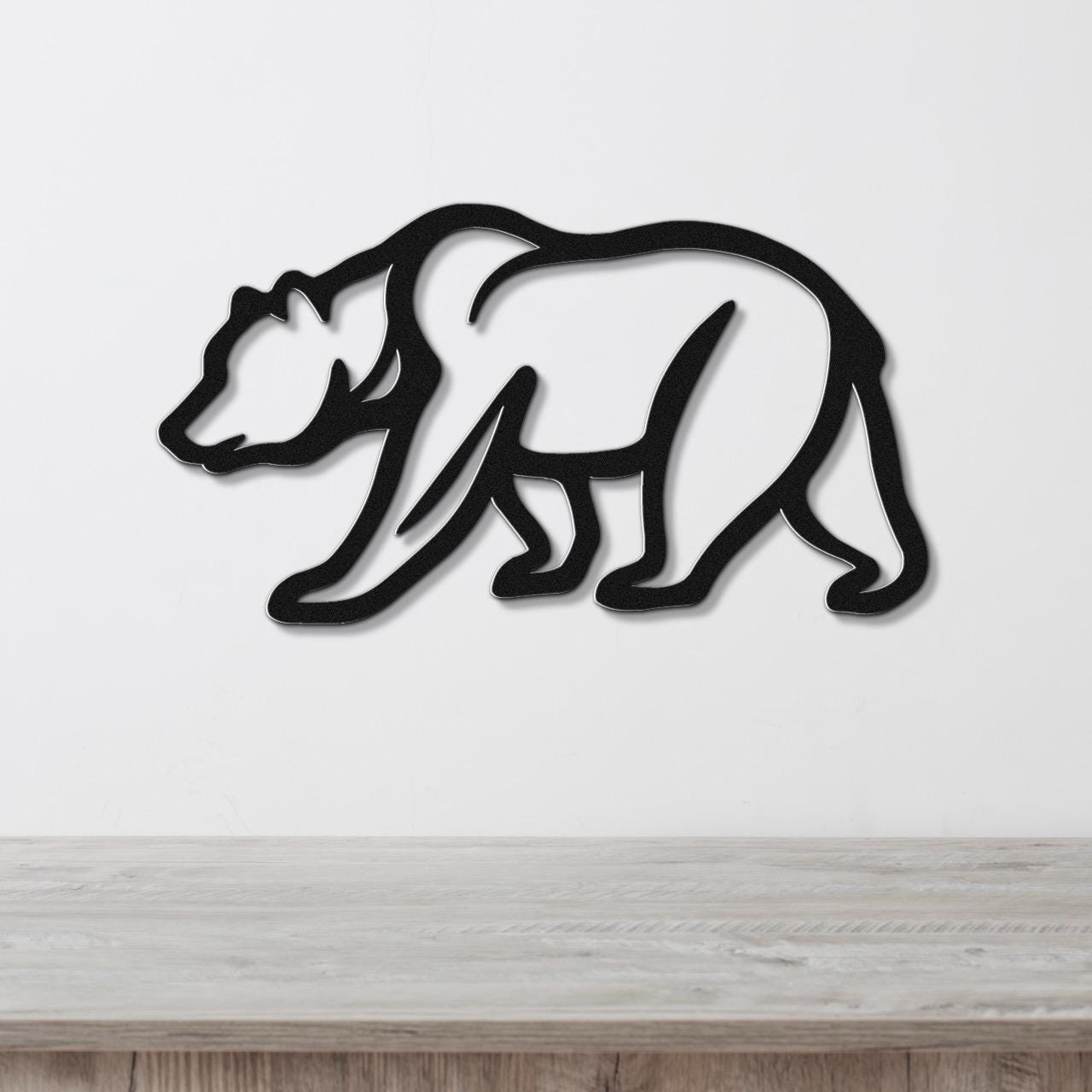 Black metal bear wall art with a silhouette cutout design, mounted on a white wall above a light wood surface.