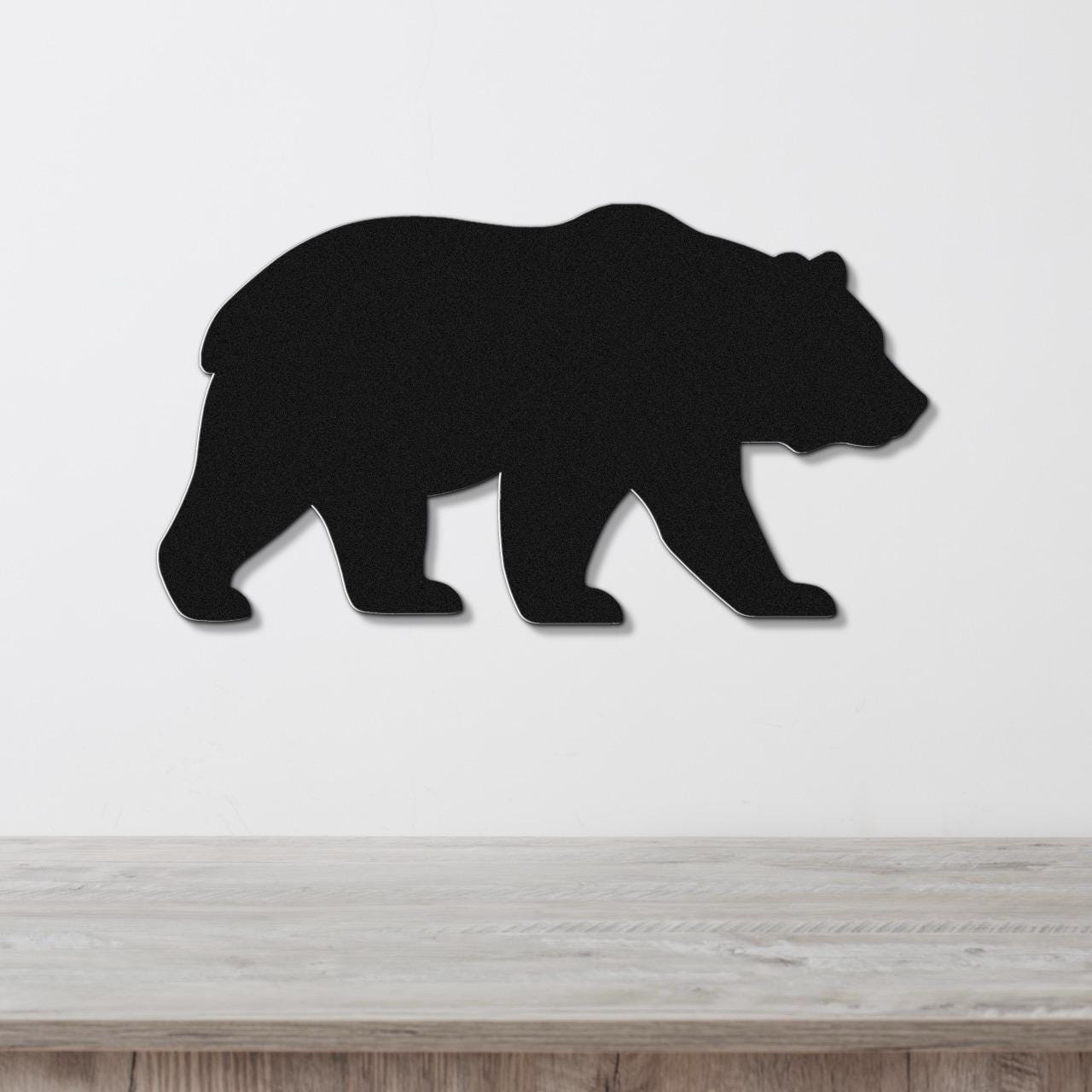 Black metal bear silhouette wall art, mounted on a white wall above a light wood countertop.