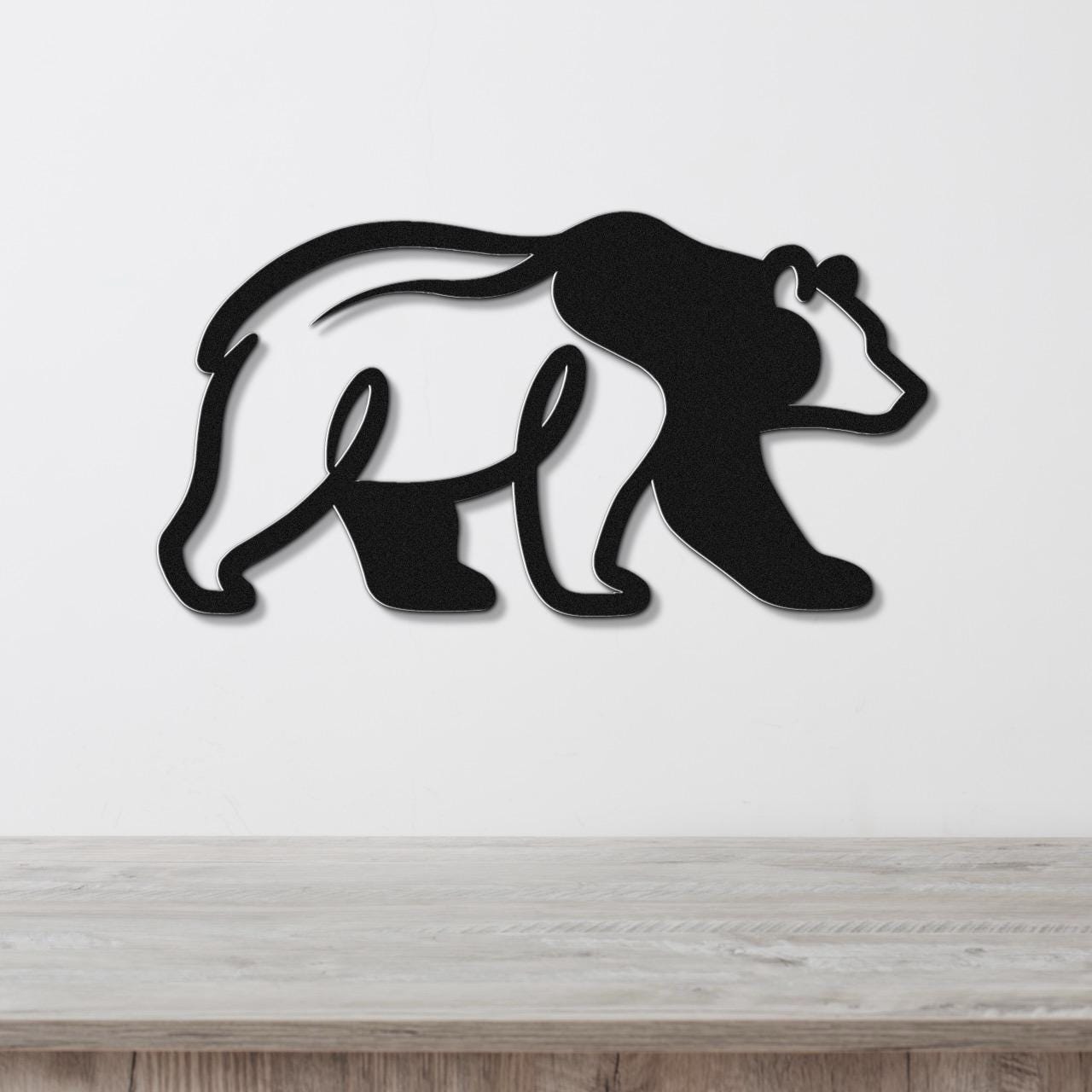 Black metal bear wall art with a cutout silhouette design, mounted on a white wall above a wooden surface.