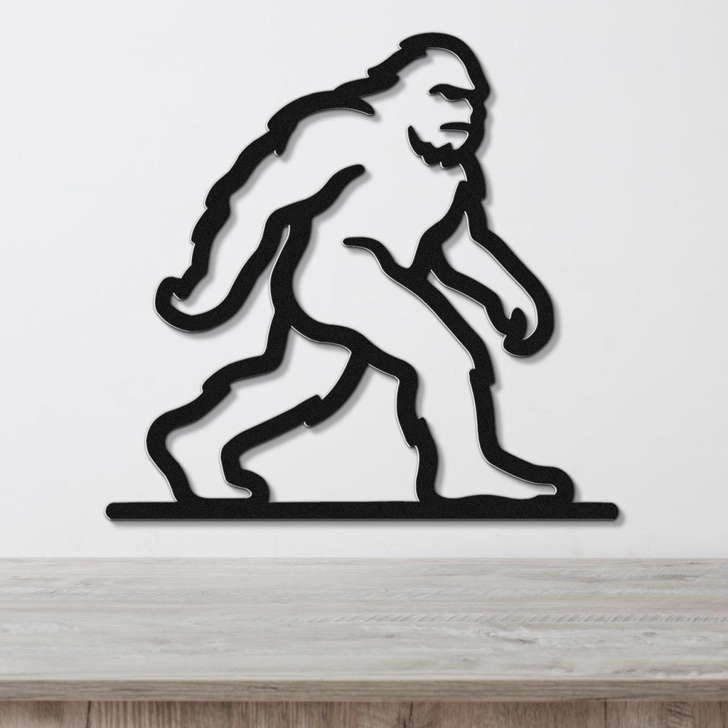Black metal wall art silhouette of Bigfoot in a walking pose, mounted on a white wall above a wooden surface.