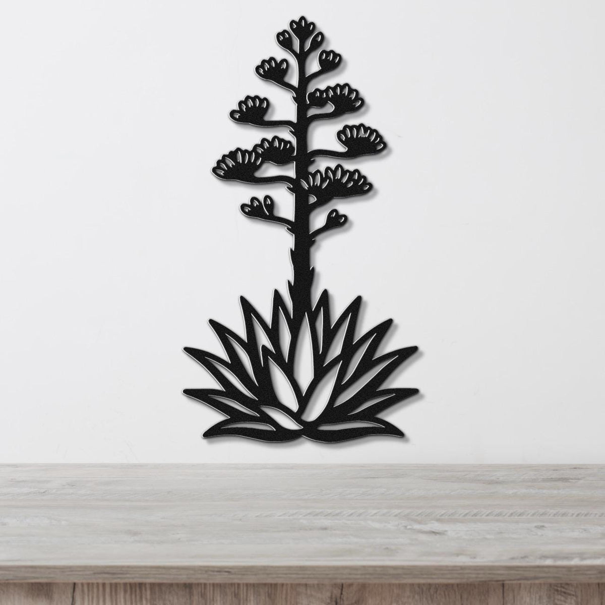 Black metal agave wall sculpture with blooming flower cutouts, mounted on a white wall above a light wood counter.
