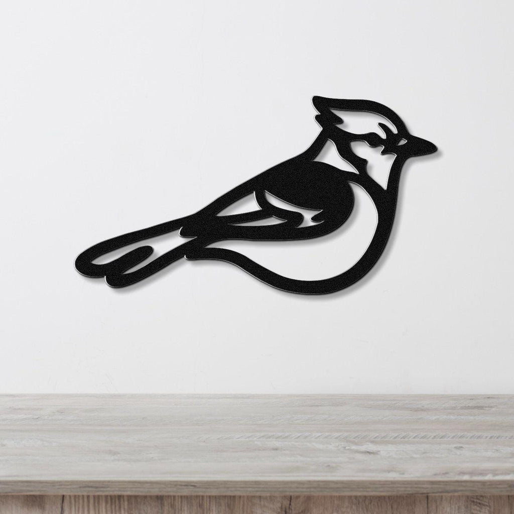 Black metal blue jay wall art silhouette with internal cutout details, mounted on a white wall above a light wood surface.