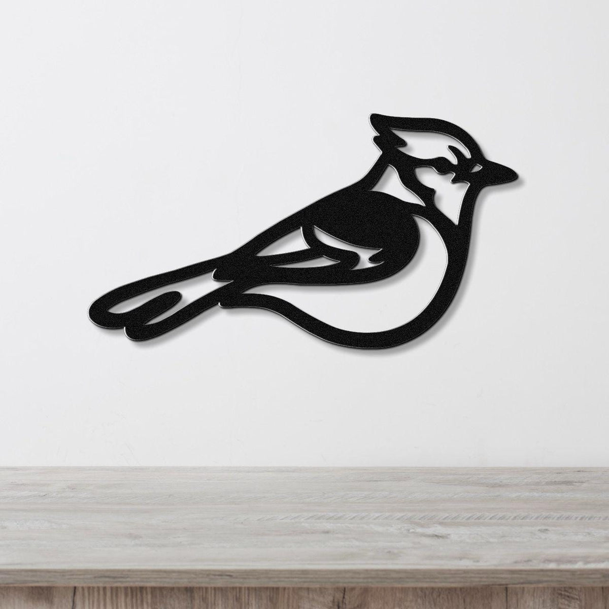 Black metal blue jay wall art silhouette with internal cutout details, mounted on a white wall above a light wood surface.