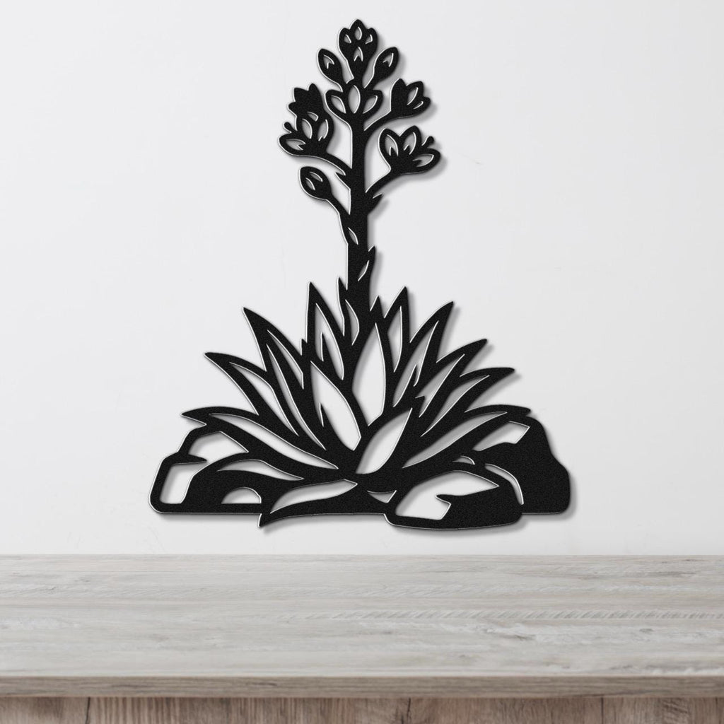 Black metal wall art in a cutout silhouette of a blooming agave plant with spiky leaves and flower stalk, mounted on a white wall above a wooden surface.