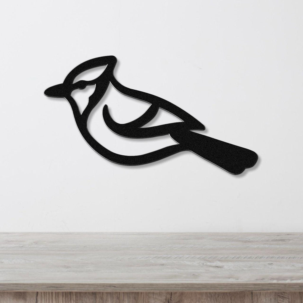 Black metal blue jay wall art with internal cutout details, mounted on a white wall above a light wood surface.