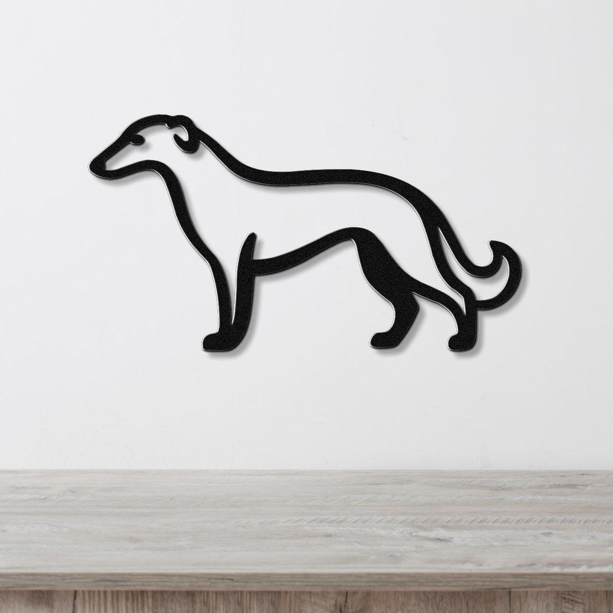 Black metal Borzoi dog wall art silhouette with a curved tail, mounted on a white wall above a light wood surface.