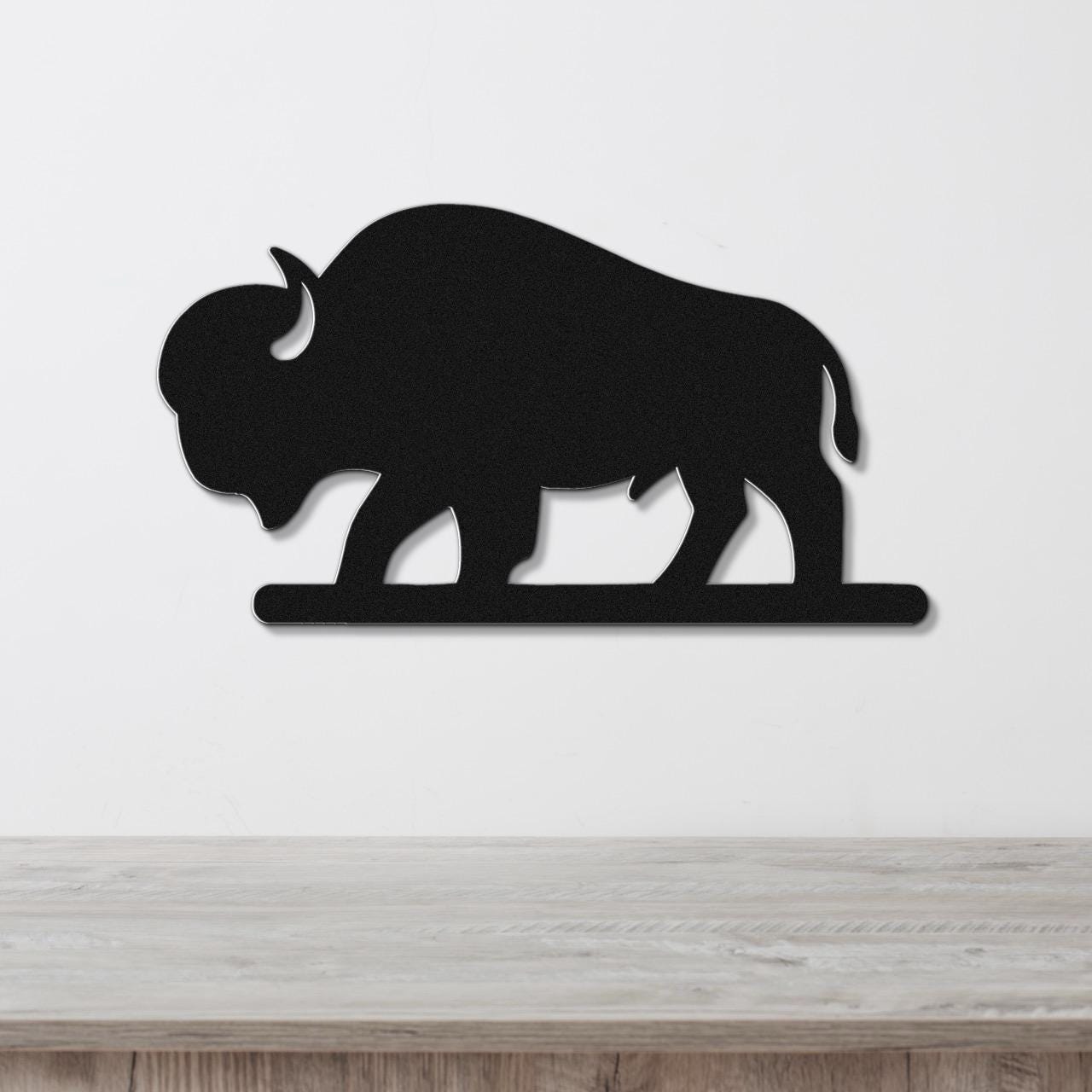 Black metal bison silhouette wall art with cutout details, mounted on a white wall above a wooden surface.