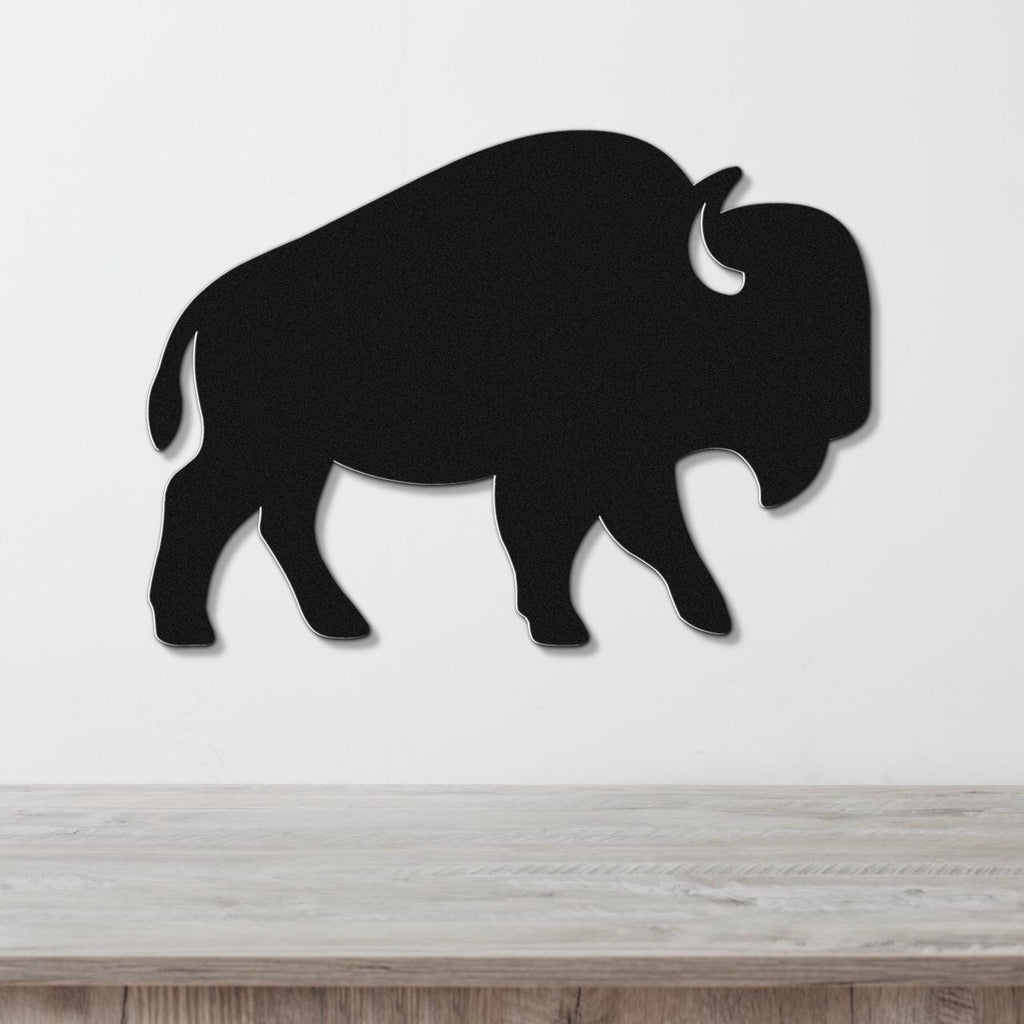 Black metal buffalo wall art silhouette with horn and tail cutouts, mounted on a white wall above a light wood counter.