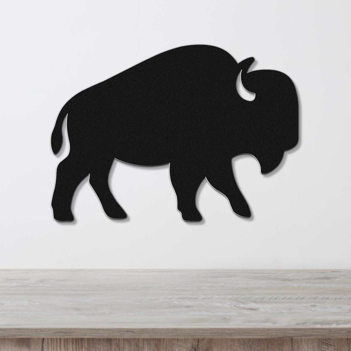 Black metal buffalo wall art silhouette with horn and tail cutouts, mounted on a white wall above a light wood counter.