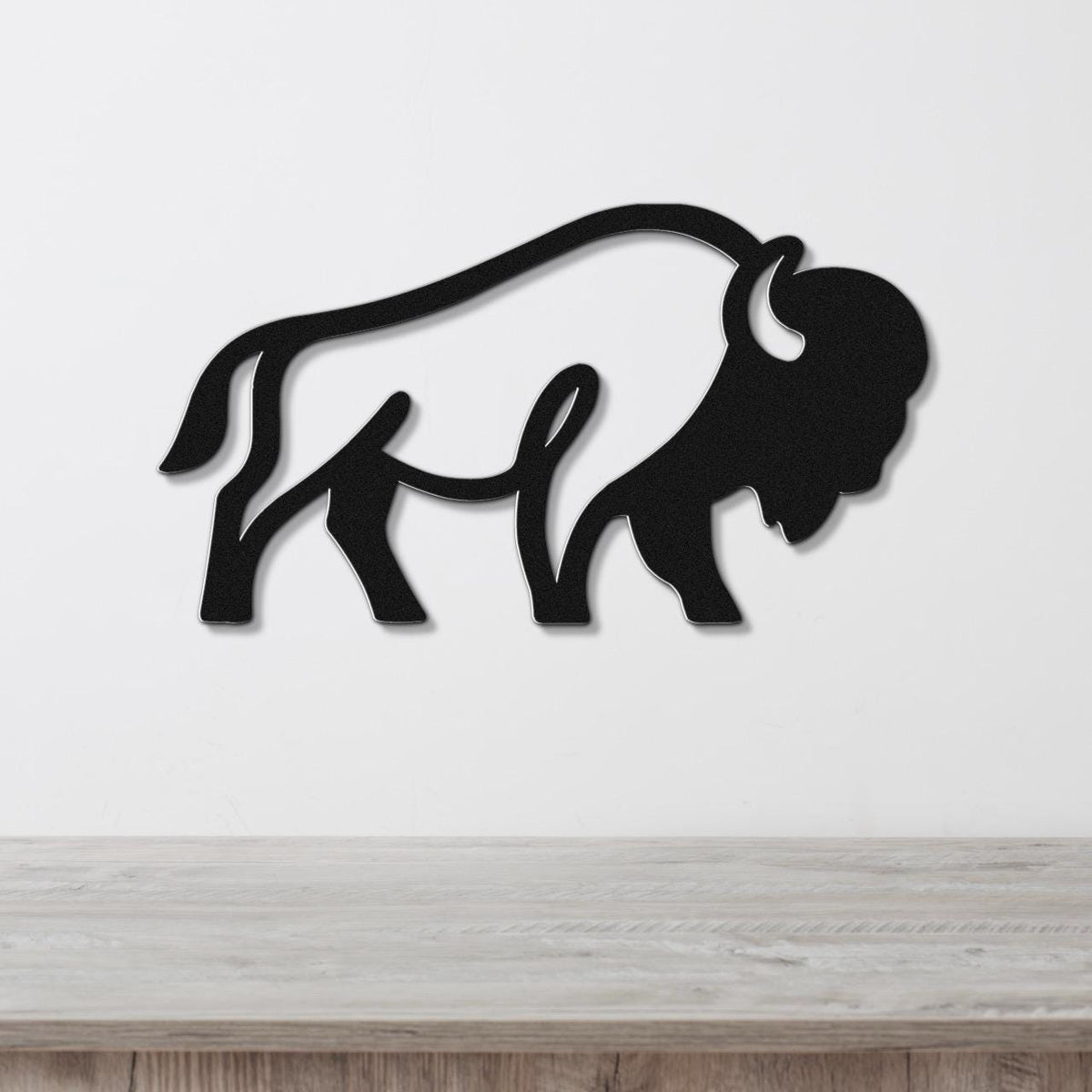 Black metal bison silhouette wall art with cutout horns and tail, mounted on a white wall above a light wood counter.