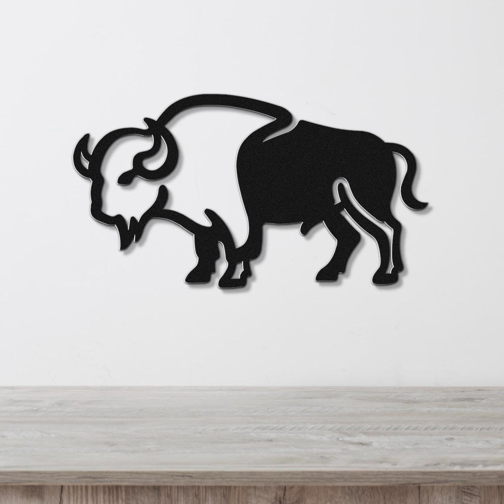 Black metal buffalo wall art silhouette with cutout horns and mane, mounted on a white wall above a light wood surface.