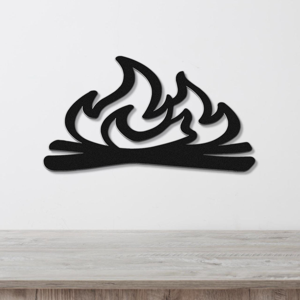 Black metal wall art with a flame and log silhouette, mounted on a white wall above a light wood surface.