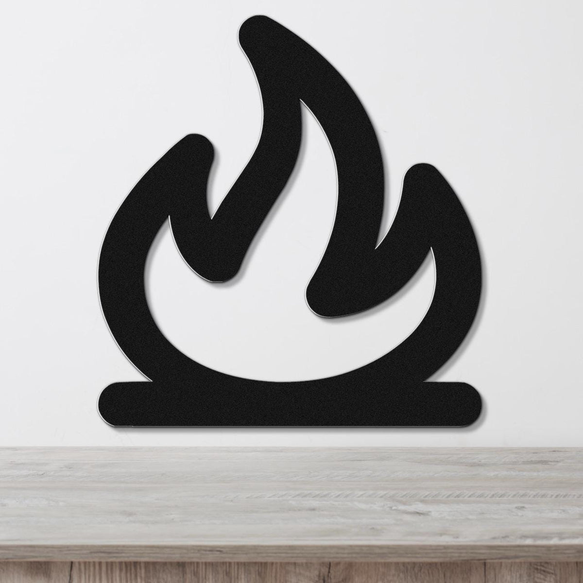 Black metal wall art in a flame silhouette design, mounted on a white wall above a light wood surface.