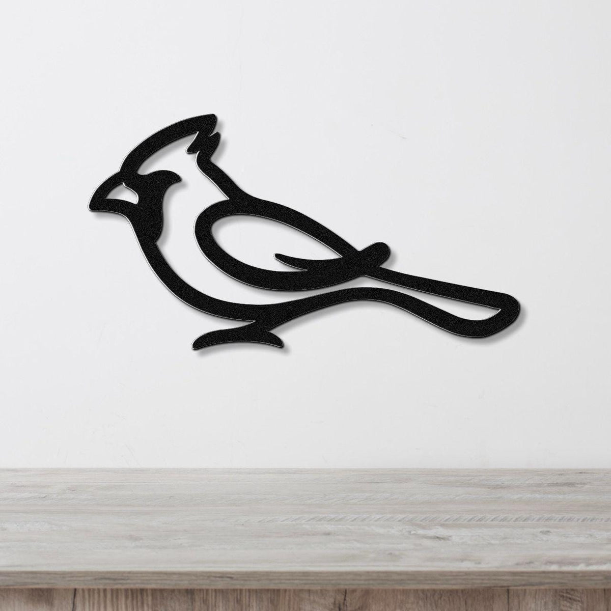 Black metal cardinal wall art with a bold silhouette and internal cutout details, mounted on a white wall above a light wood surface.