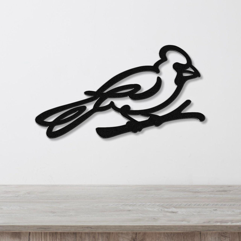 Black metal cardinal wall art with a minimalist silhouette design, mounted on a white wall above a light wood surface.