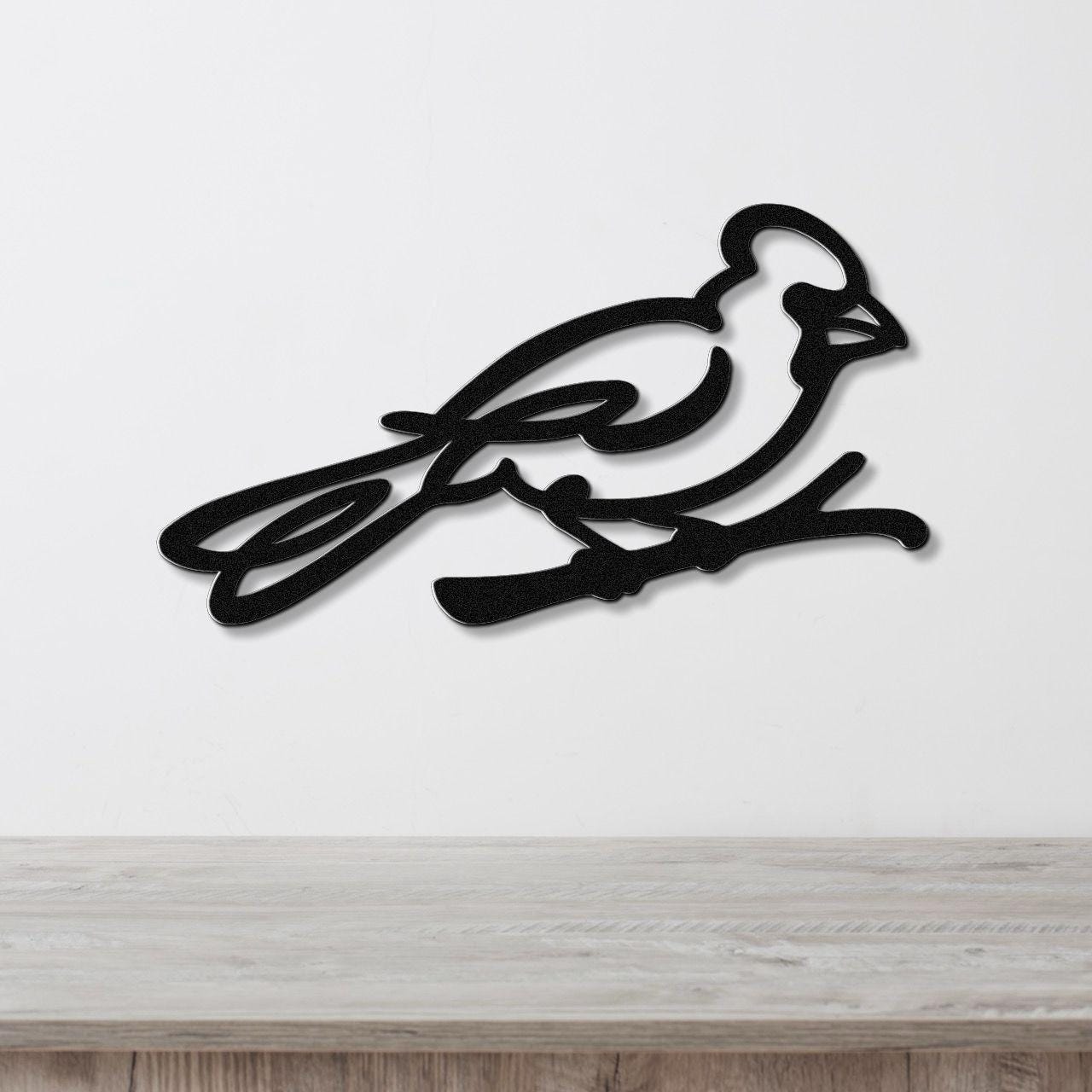 Black metal cardinal wall art with a minimalist silhouette design, mounted on a white wall above a light wood surface.