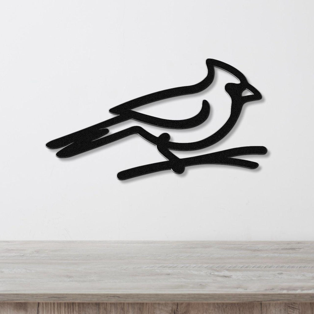 Black metal cardinal wall art in a minimalist silhouette style, perched on a branch cutout, mounted on a white wall above a light wood counter.