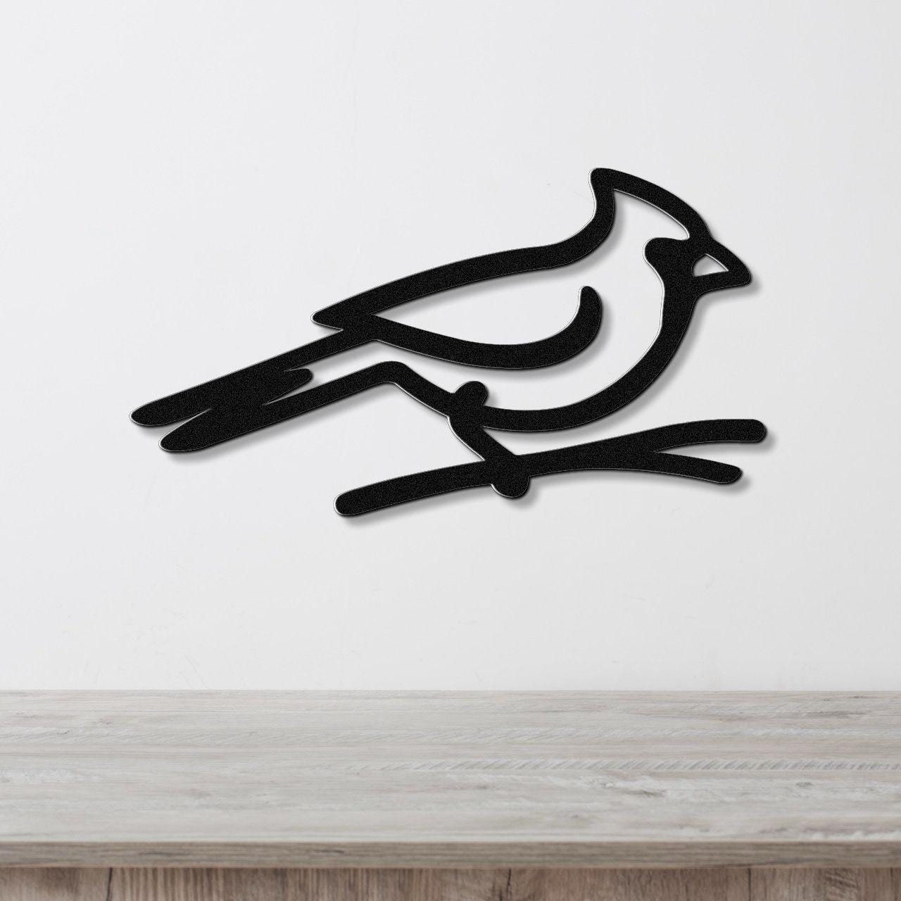 Black metal cardinal wall art in a minimalist silhouette style, perched on a branch cutout, mounted on a white wall above a light wood counter.